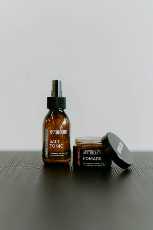 Two apothecary hair products on a dark surface.