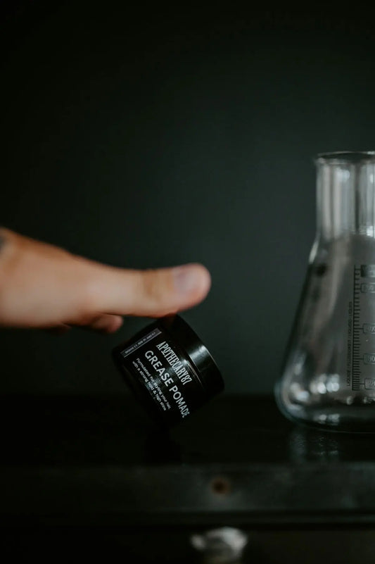 Hand holding a jar of grease pomade near flask